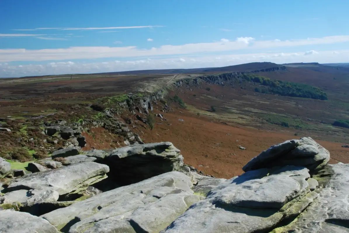 Wide view of gritstone escarpment and patchwork fields in the Peak District at golden light